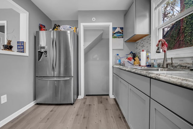 19631 Dwyer St, Detroit, MI 48234 - kitchen featuring light wood-style floors, baseboards, stainless steel refrigerator with ice dispenser, tasteful backsplash, and a sink
