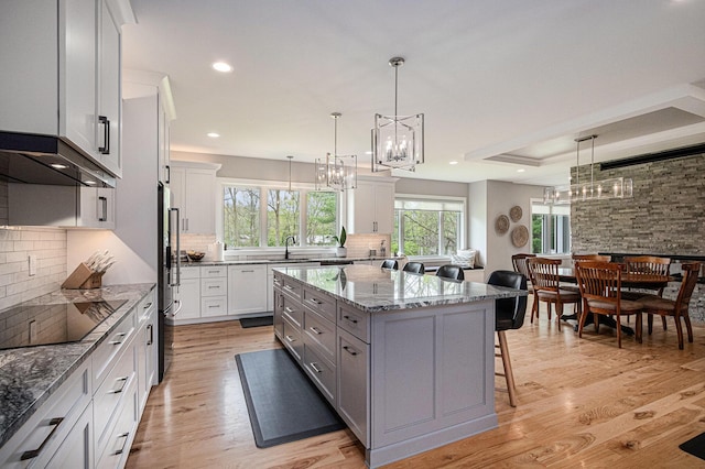 kitchen featuring a notable chandelier, light stone counters, a breakfast bar, backsplash, and a kitchen island
