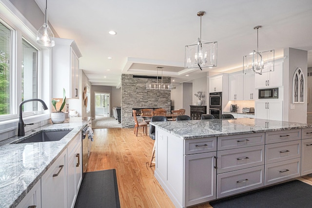 kitchen featuring white cabinets, a notable chandelier, appliances with stainless steel finishes, a sink, and light wood-type flooring