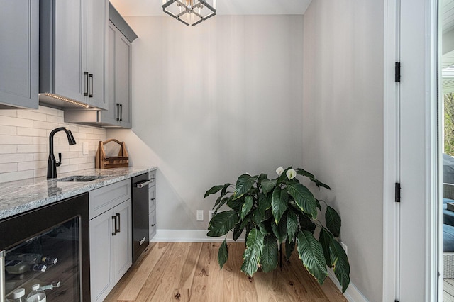 bar featuring wine cooler, baseboards, light wood-type flooring, tasteful backsplash, and a sink