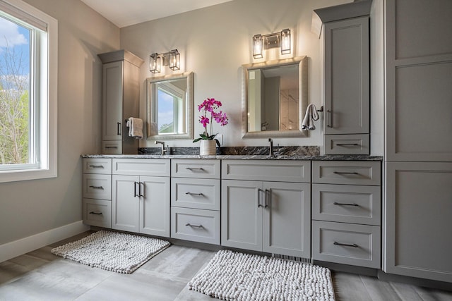 bathroom with double vanity, baseboards, a sink, and wood finished floors