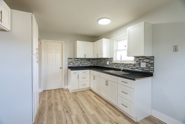 kitchen featuring a sink, decorative backsplash, light wood-type flooring, dark countertops, and white cabinetry
