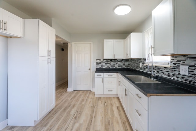 kitchen with a sink, tasteful backsplash, dark countertops, white cabinets, and light wood-style floors