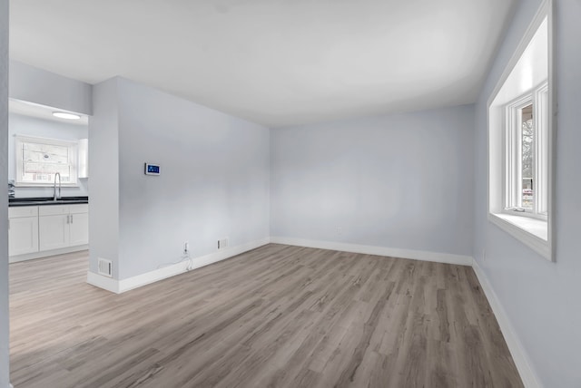 spare room with light wood-style floors, a sink, and baseboards