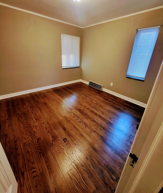 empty room with crown molding, baseboards, wood finished floors, and visible vents