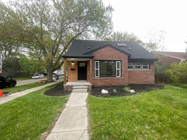bungalow-style home with roof with shingles, a front yard, and brick siding