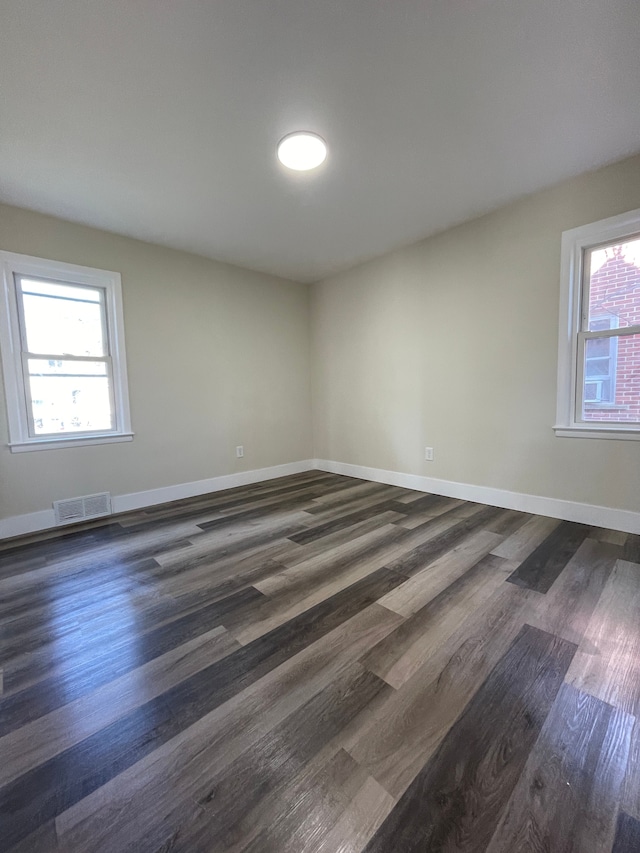 spare room with baseboards, visible vents, and dark wood-style floors