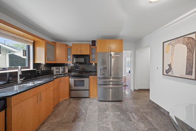 kitchen with appliances with stainless steel finishes, a sink, decorative backsplash, glass insert cabinets, and stone finish floors