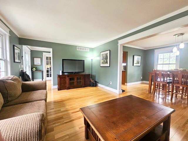 living room featuring baseboards, visible vents, ornamental molding, and light wood-type flooring