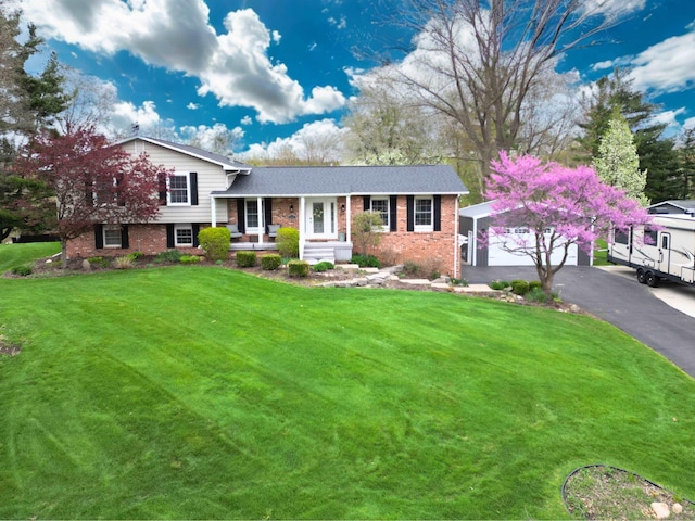 tri-level home with covered porch, brick siding, a detached garage, and a front lawn