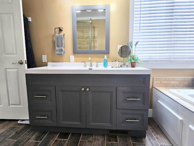 full bath featuring visible vents, wood finished floors, vanity, and a tub to relax in