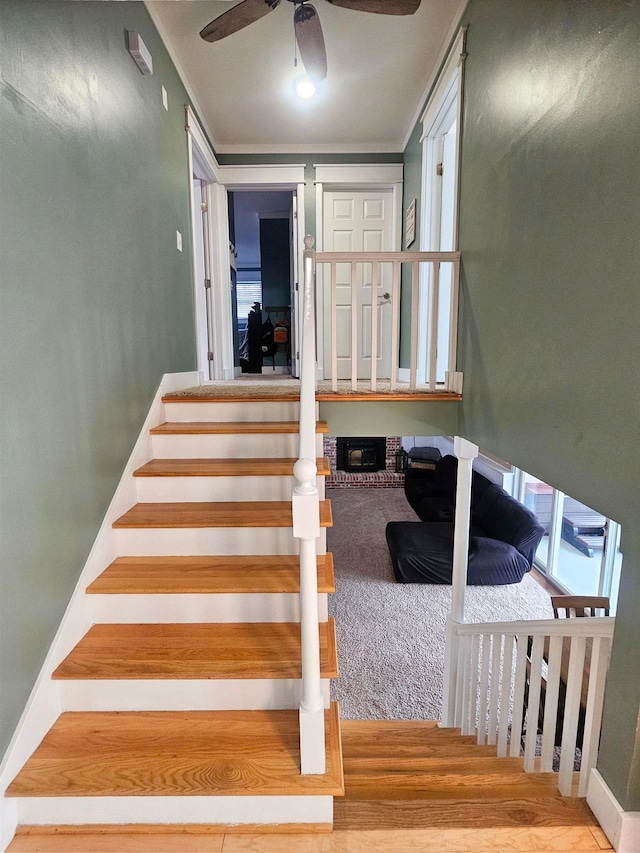 stairs featuring a brick fireplace and ceiling fan