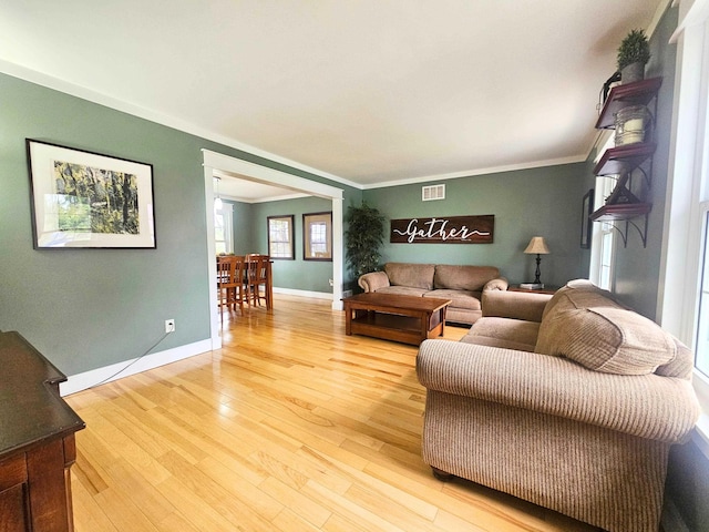 living room featuring baseboards, visible vents, ornamental molding, and light wood finished floors