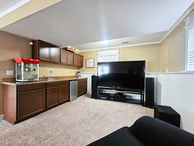 interior space with light colored carpet, indoor wet bar, a wainscoted wall, and visible vents