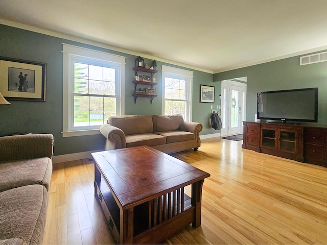 living room with crown molding, plenty of natural light, visible vents, and light wood-type flooring