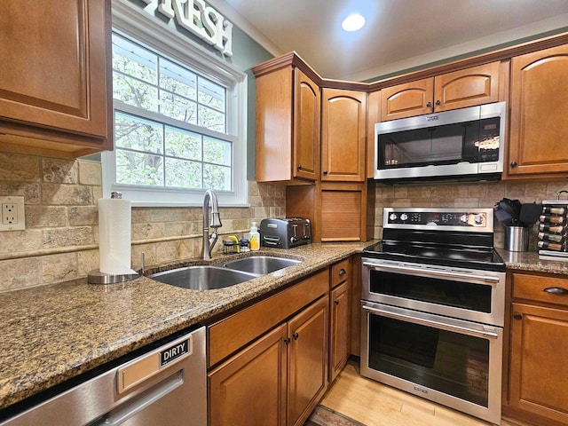 kitchen featuring tasteful backsplash, brown cabinetry, a sink, dark stone counters, and appliances with stainless steel finishes