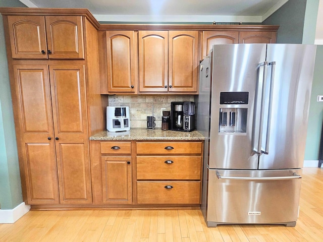 kitchen featuring light wood-style floors, light stone countertops, stainless steel refrigerator with ice dispenser, and brown cabinets