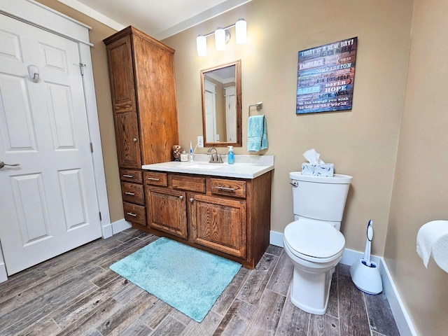 half bathroom with vanity, toilet, wood finished floors, and baseboards