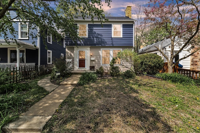 view of front facade featuring fence, a chimney, and a front lawn