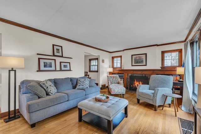 living room featuring ornamental molding, light wood finished floors, a brick fireplace, and a healthy amount of sunlight