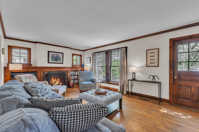 living room featuring crown molding, light wood-style flooring, visible vents, and a lit fireplace
