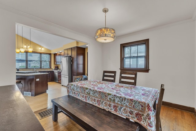 dining space with light wood-type flooring, baseboards, crown molding, and visible vents