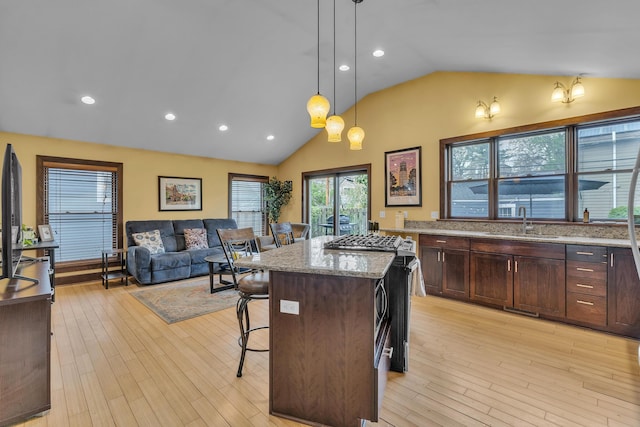 kitchen with dark brown cabinetry, light stone countertops, a kitchen breakfast bar, a sink, and decorative light fixtures