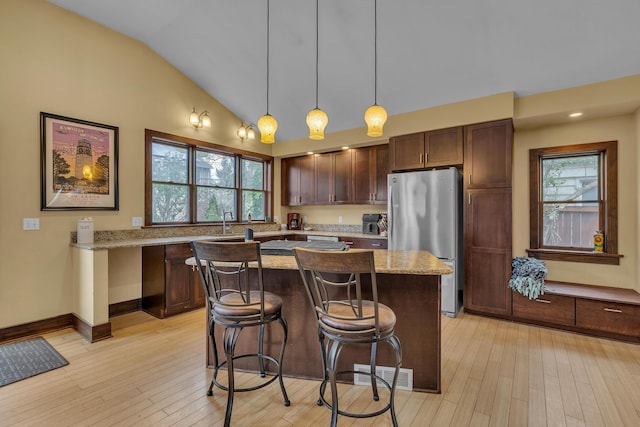 kitchen with visible vents, freestanding refrigerator, a kitchen island, a kitchen breakfast bar, and vaulted ceiling