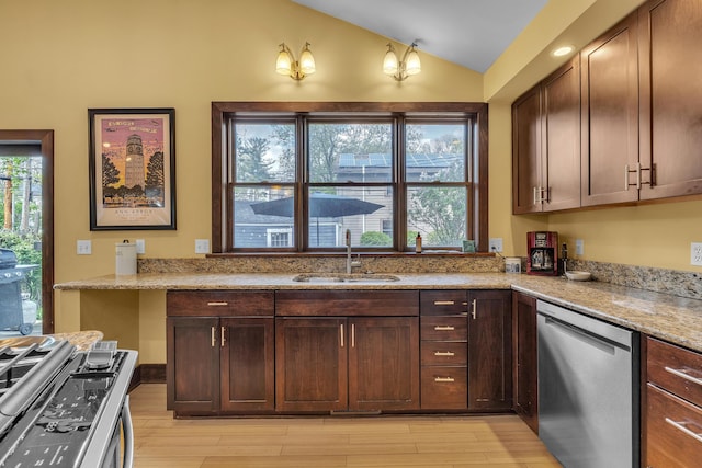 kitchen featuring light stone countertops, a sink, light wood-style flooring, appliances with stainless steel finishes, and vaulted ceiling