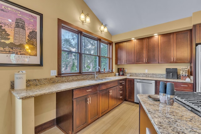 kitchen featuring light stone countertops, a sink, light wood finished floors, vaulted ceiling, and stainless steel appliances
