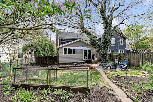 back of house with fence, a garden, and an outdoor fire pit
