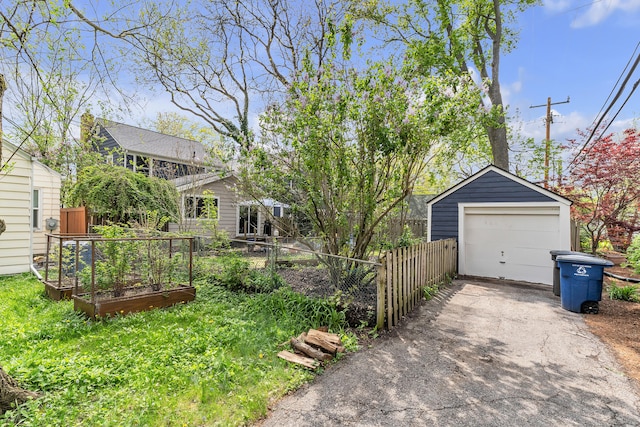 exterior space with fence, aphalt driveway, a detached garage, an outbuilding, and a garden