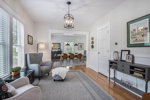 living area featuring an inviting chandelier, a wainscoted wall, and wood finished floors