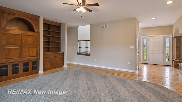 unfurnished living room featuring visible vents, wood finished floors, baseboards, built in shelves, and a ceiling fan