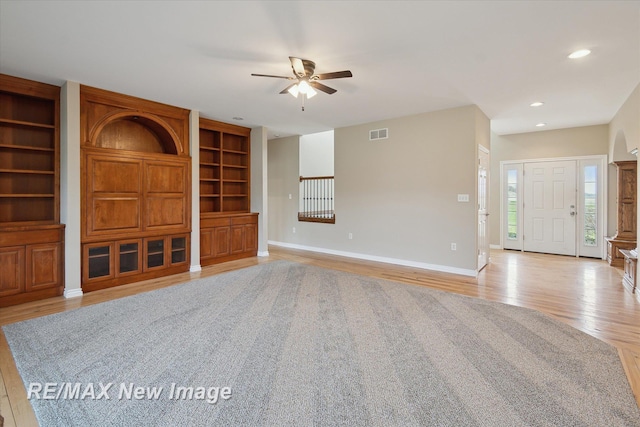 unfurnished living room with built in features, light wood-style flooring, a ceiling fan, baseboards, and visible vents