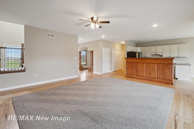 unfurnished living room with visible vents, a ceiling fan, recessed lighting, light wood-type flooring, and arched walkways