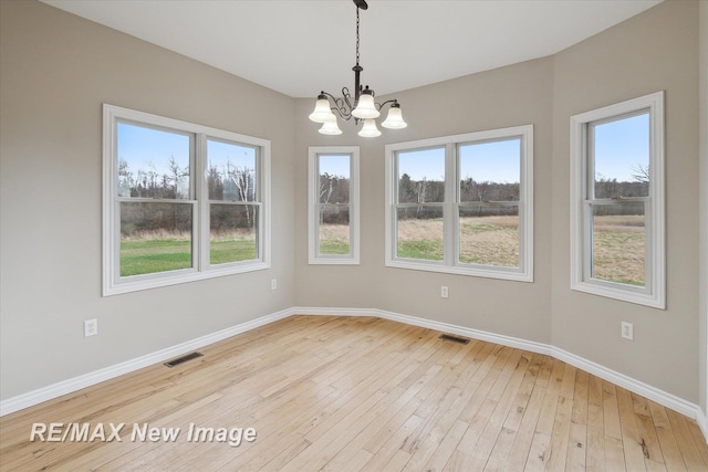 unfurnished dining area with visible vents, baseboards, a chandelier, and light wood-style floors