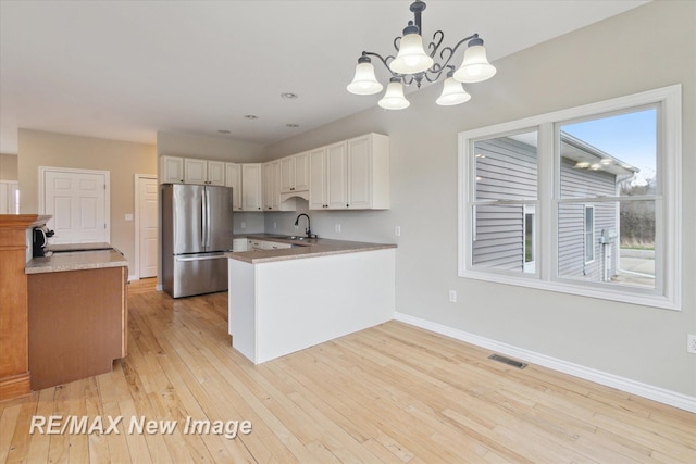 kitchen featuring visible vents, a sink, freestanding refrigerator, a peninsula, and a chandelier