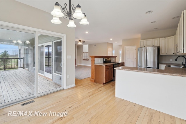 kitchen featuring a sink, light wood-style flooring, stainless steel appliances, a peninsula, and visible vents