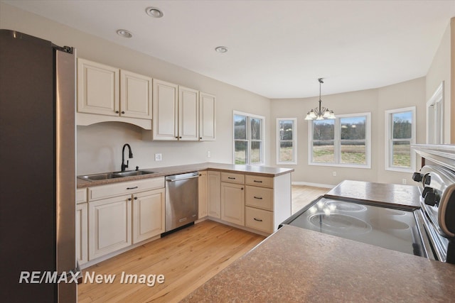 kitchen with pendant lighting, light wood-type flooring, a sink, appliances with stainless steel finishes, and a notable chandelier