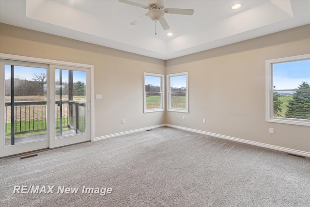 carpeted spare room featuring a raised ceiling, baseboards, ceiling fan, and visible vents