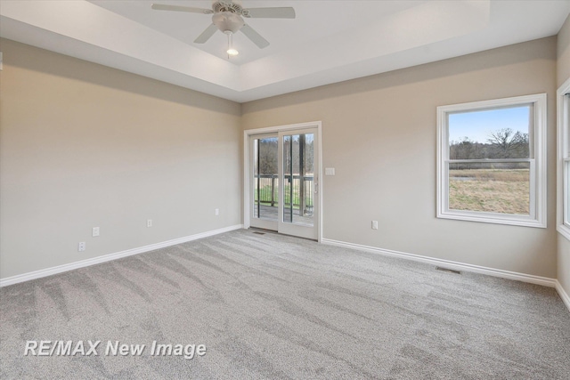 carpeted spare room with a healthy amount of sunlight, baseboards, ceiling fan, and a tray ceiling