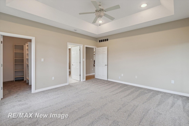 unfurnished bedroom featuring visible vents, baseboards, a raised ceiling, a spacious closet, and carpet flooring