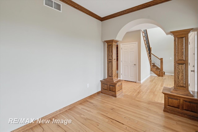 spare room with ornamental molding, decorative columns, stairs, arched walkways, and light wood finished floors