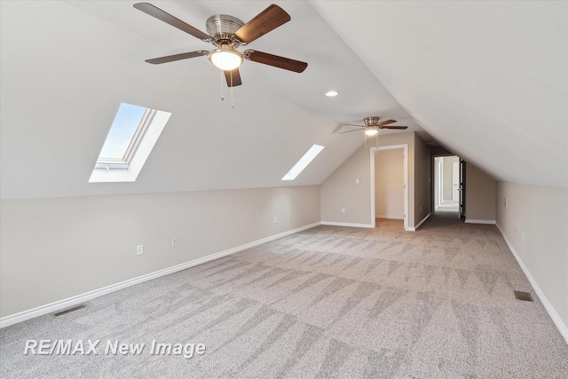 additional living space featuring vaulted ceiling with skylight, a ceiling fan, visible vents, baseboards, and carpet flooring