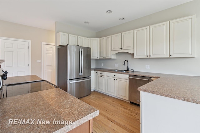 kitchen with light wood-style floors, recessed lighting, white cabinets, a sink, and appliances with stainless steel finishes