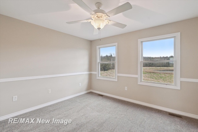 carpeted empty room with baseboards, a ceiling fan, and visible vents