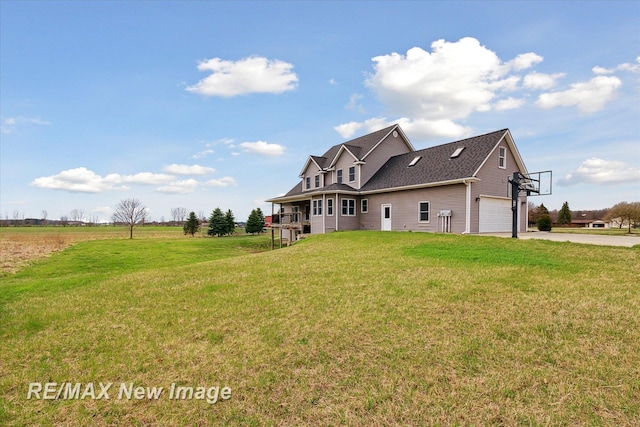 back of property with roof with shingles, an attached garage, a yard, and driveway