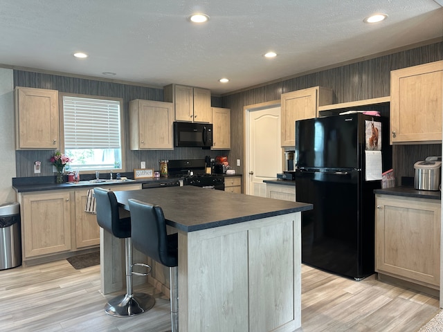 kitchen featuring dark countertops, light brown cabinets, a center island, and black appliances