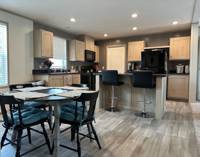 kitchen with a breakfast bar area, dark countertops, light wood-type flooring, black appliances, and recessed lighting